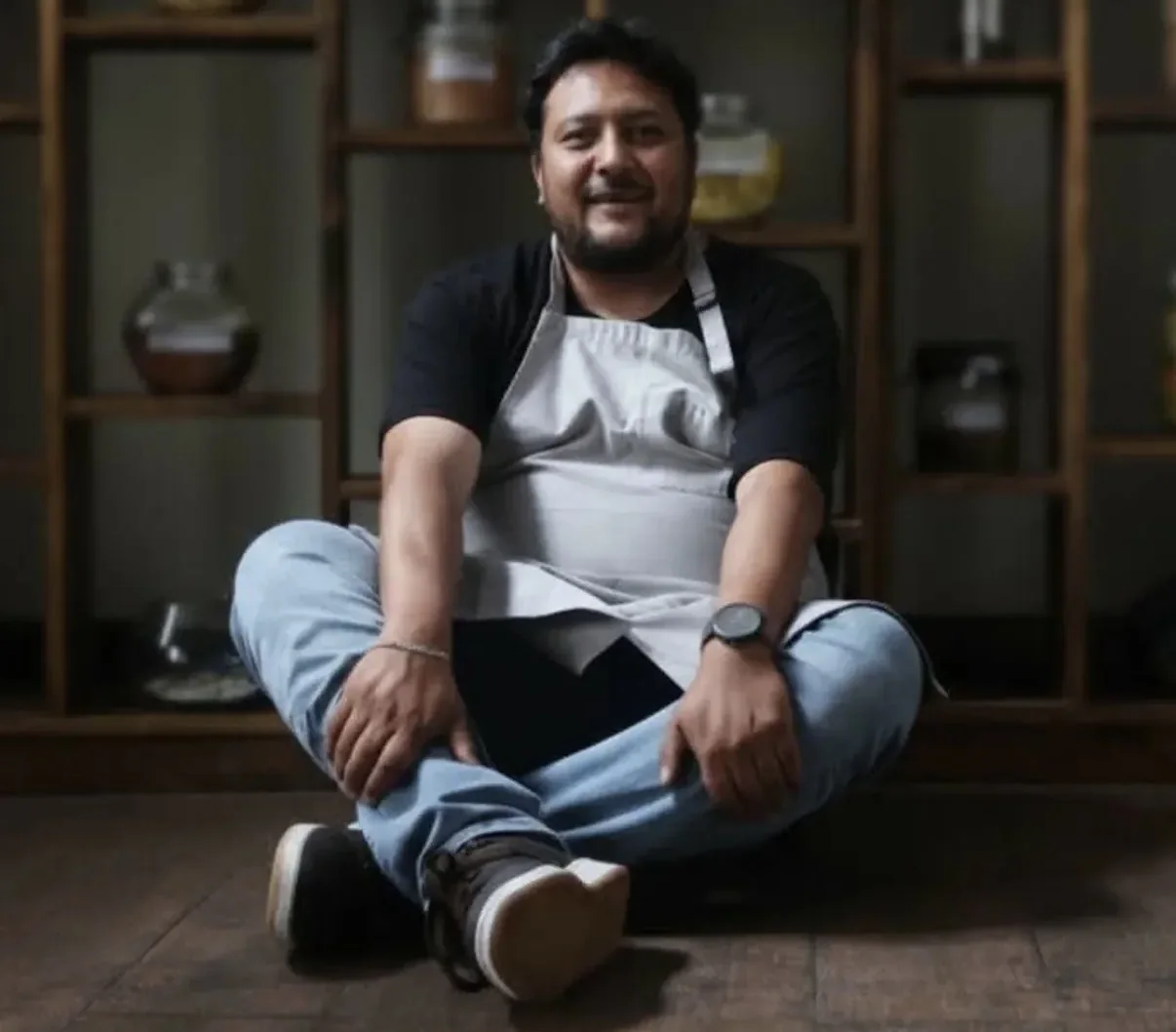 El chef Pablo Gumiel sentado en el piso frente a la despensa de frascos de Nativa