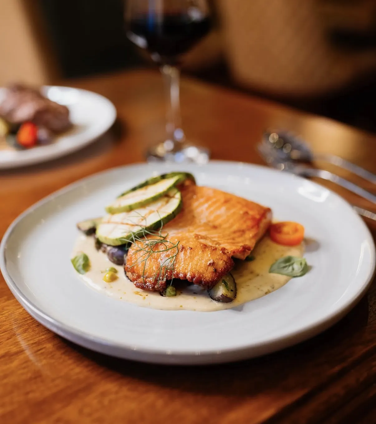 Plato de pescado dorado con zucchini servido en la mesa con copa de vino