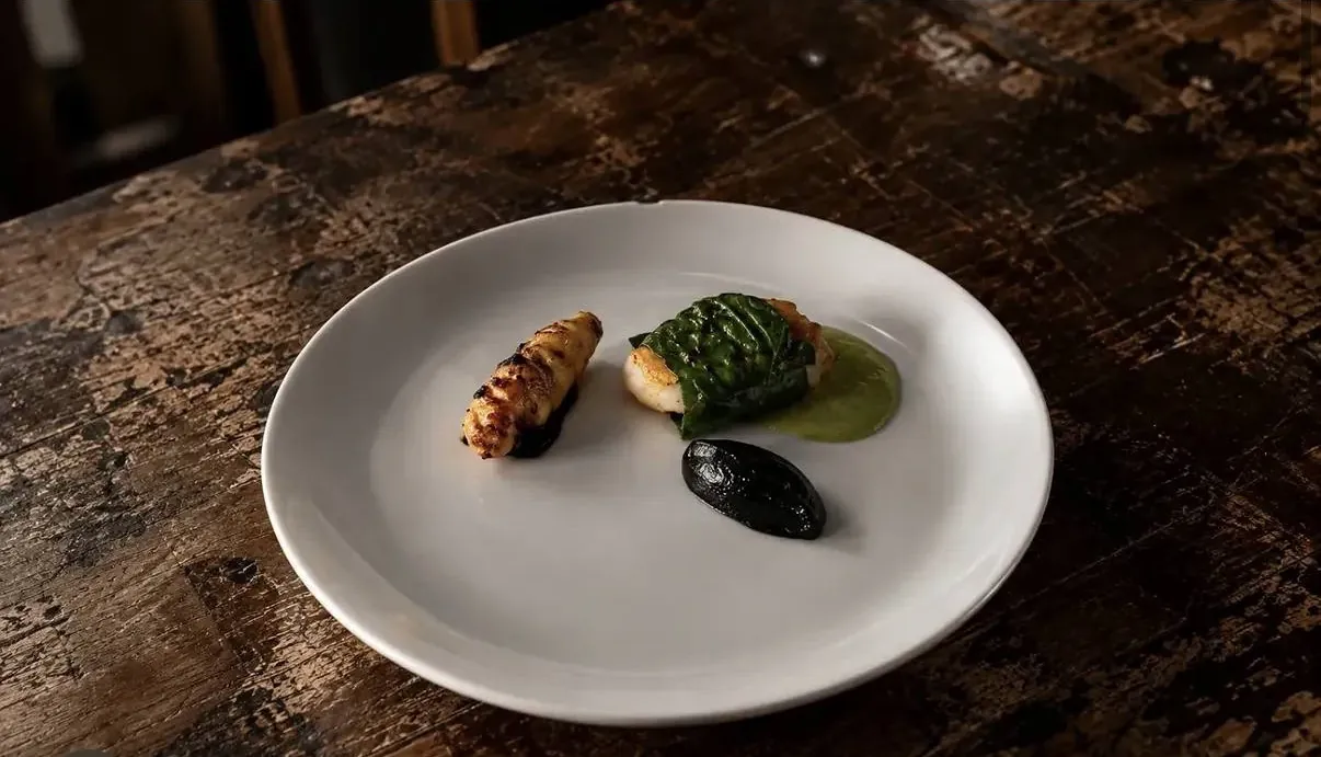 Paiche a la brasa con puré oscuro y crema verde